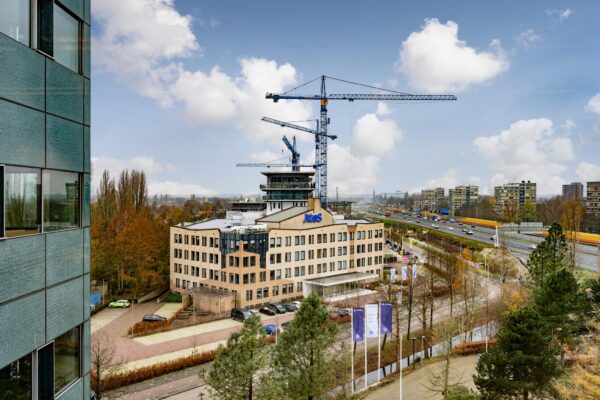 Kantoorgebouw van Atos aan de Burgemeester Rijnderslaan in Amstelveen met bouwkranen op het dak en zicht op de snelweg A9.